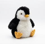 A plush alpaca toy penguin with black and white fur, a yellow beak, and yellow feet, sitting against a seamless white background.