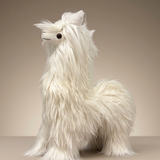 A fluffy white alpaca plush toy with long shaggy fur, small black eyes, and a stitched black nose, standing against a plain beige studio background.