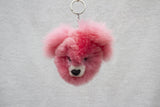 A pink alpaca fur keychain in the shape of a bear with black eyes and nose.